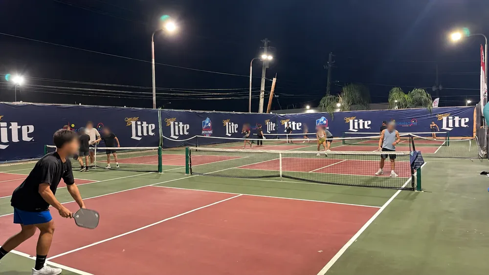 Wide nighttime view of oversized banners installed around pickleball courts